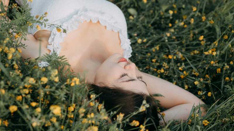 A young woman in a white dress lies peacefully in a field of yellow flowers, exuding tranquility and beauty., tags: und - pexel